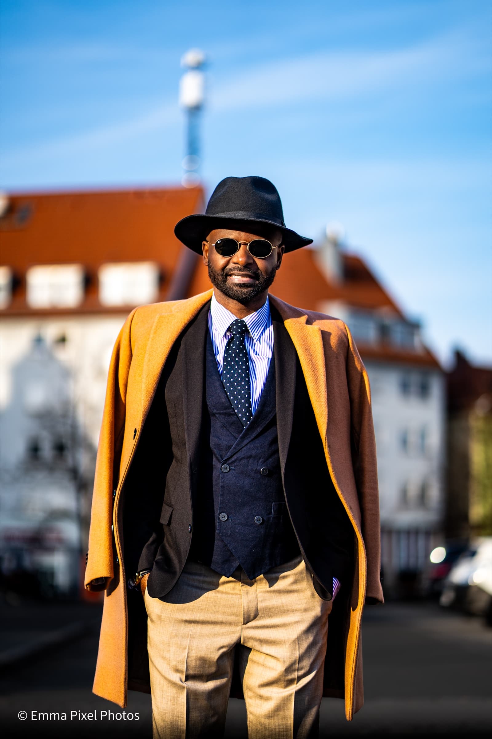 Front-on portrait with sunglasses, mustard coat, blue sky